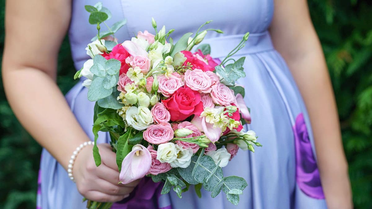 Pregnant bridesmaid wears periwinkle floral dress while holding a bouquet.