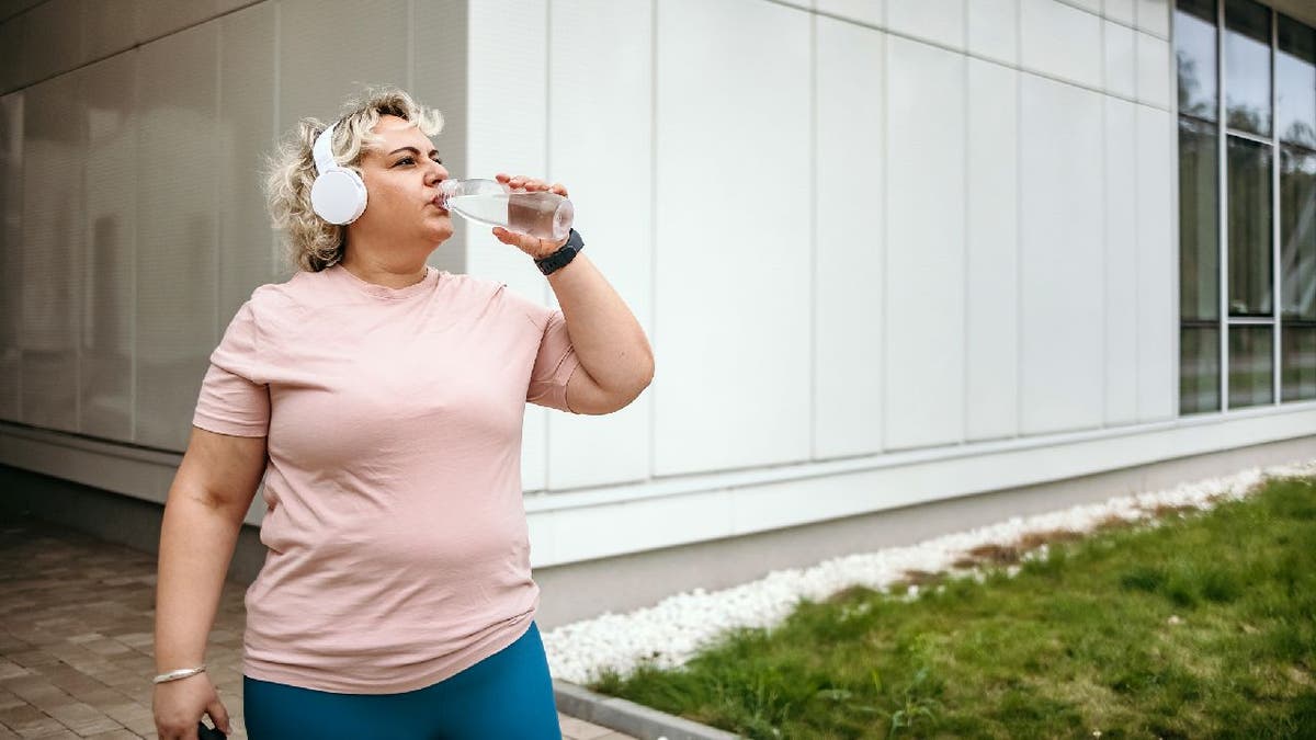 Woman in sportswear drinking water after outdoor workout.