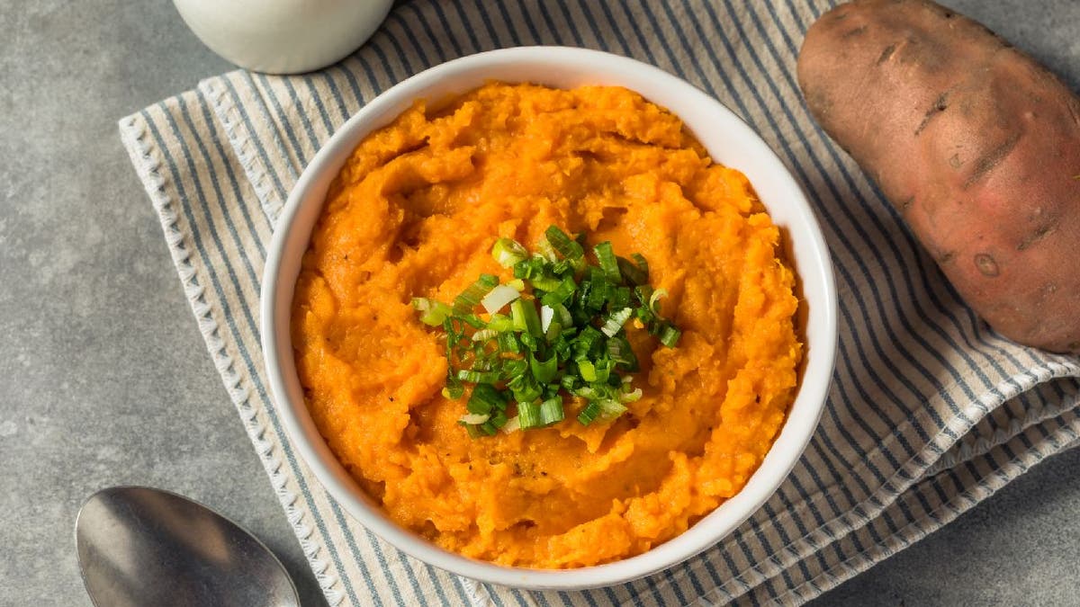 Mashed sweet potatoes served in a dish with green herbs.