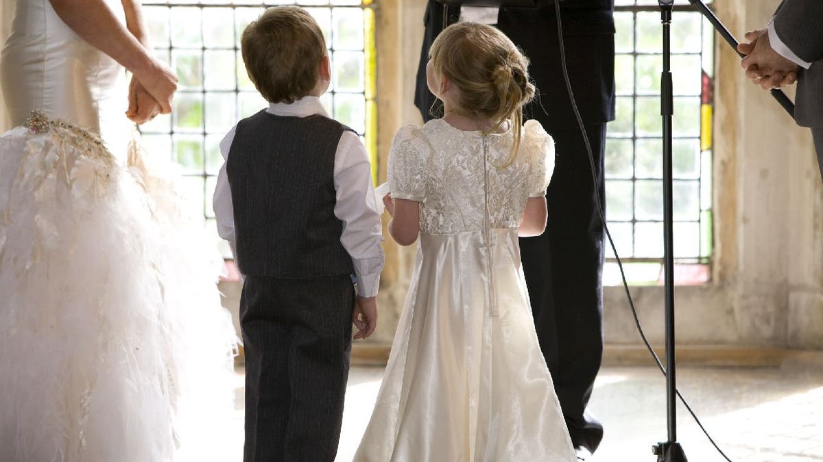 A ring bearer and flower girl stand at an altar with the bride and groom.