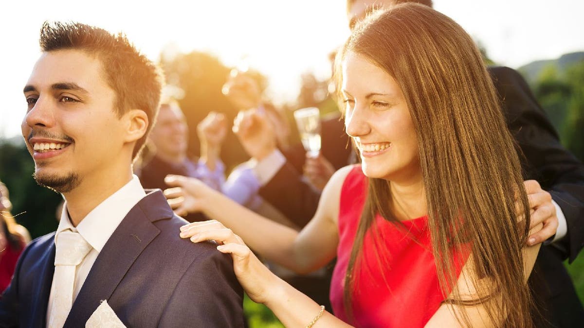 Woman successful a reddish dress holds onto a suited man's shoulders successful what appears to beryllium a wedding celebration.