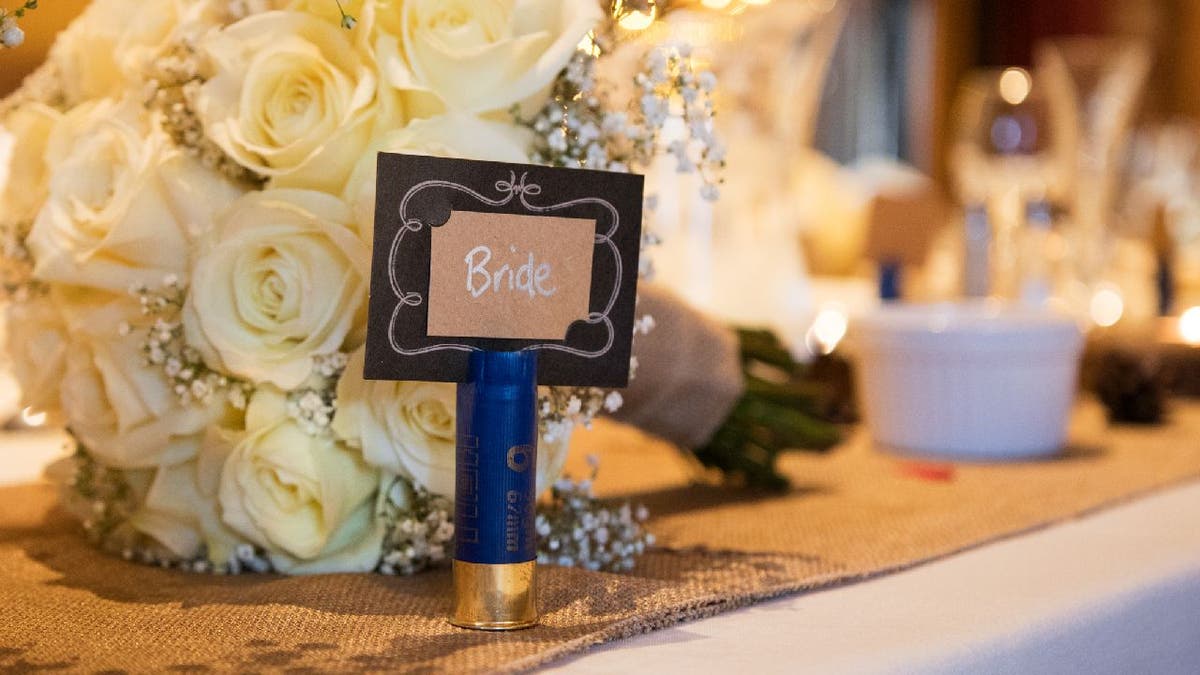 Blue shotgun shell placeholder for bride set on a table near bouquet.
