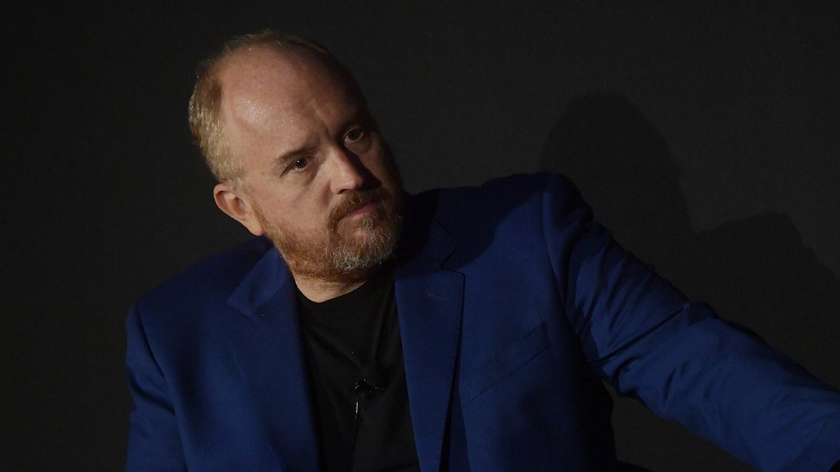 Comedian Louis C.K. wears blue blazer and black shirt on stage during panel discussion