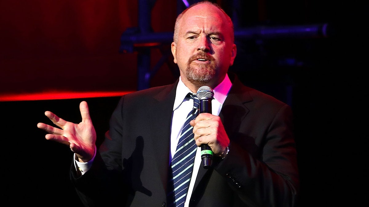 Louis CK holds a microphone while performing on stage
