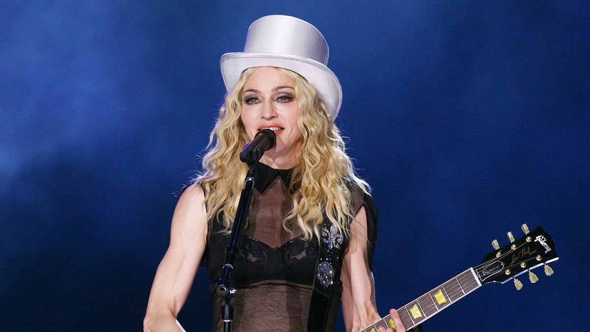 Madonna draagt ​​een witte hoed en speelt gitaar tijdens een concert