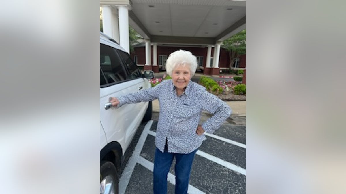 Older woman standing next to a car in front of a building grabbing a car door handle