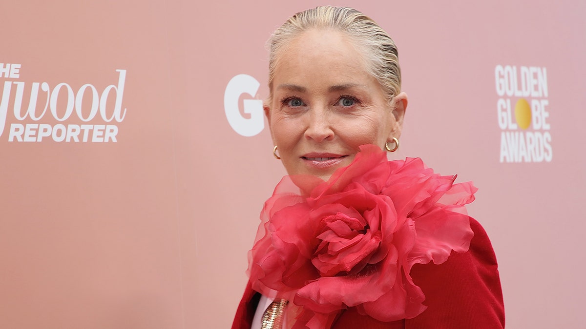 Sharon Stone guarda la telecamera con una giacca rossa con un grande fiore sulla spalla