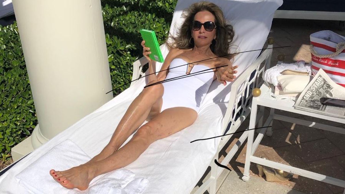 Susan Lucci lounging on a beach chairin a white one-piece 