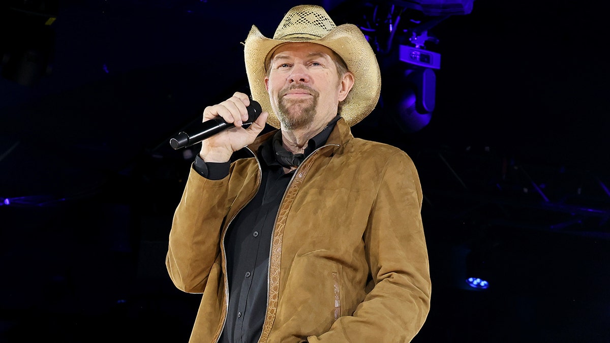 Toby Keith wears a cowboy hat and leather jacket on stage