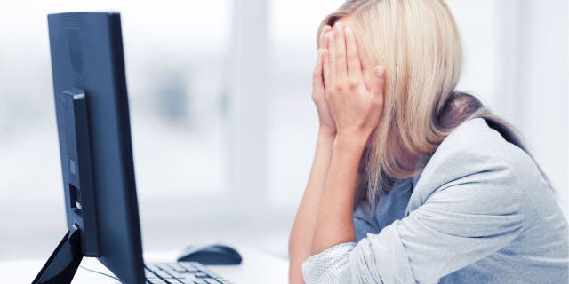 Woman with her hands over her face, sitting in front of her desktop computer.