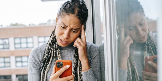 Stressed woman with hands on head, looking down at iPhone