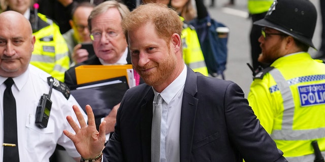 Prince Harry in a dark suit waving to a crowd