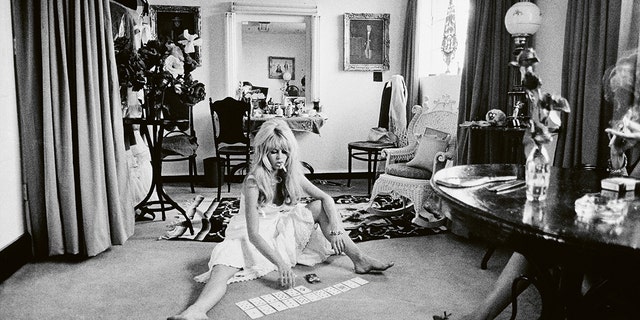 Brigitte Bardot wearing a white dress and playing cards on the floor