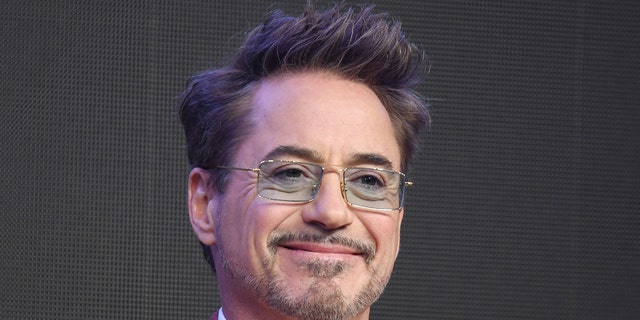 Robert Downey Jr. smiles with blue tinted retangular glasses on stage in Seoul, South Korea