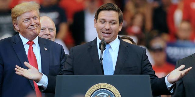 President Donald Trump looks on as Florida Governor Ron DeSantis speaks
