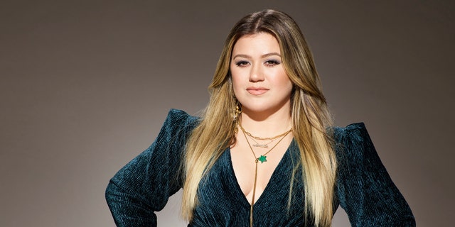 Kelly Clarkson in a green velvet dress with her hands on her hips for "The Voice" promotional pictures