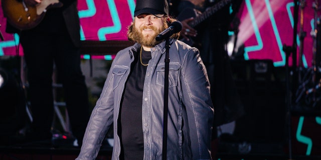 Nate Smith in a black hat and blue jacket performs on stage from the CMT Music Awards