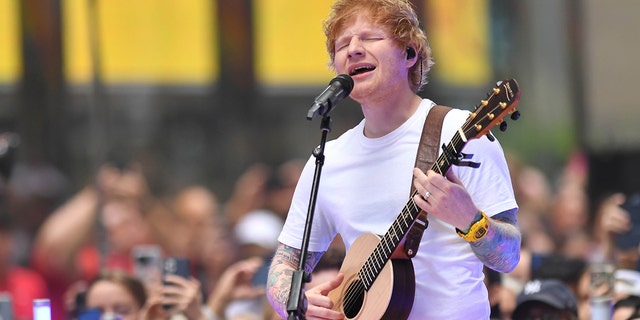 Ed Sheeran sings into the microphone while playing the guitar and closing his eyes in NYC