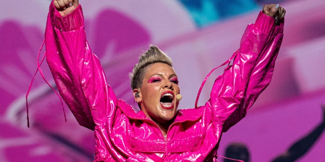 Pink throws her arms up in the air wearing a hot pink latex-like jacket while on stage