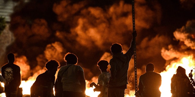 Protesters stand in front of flames