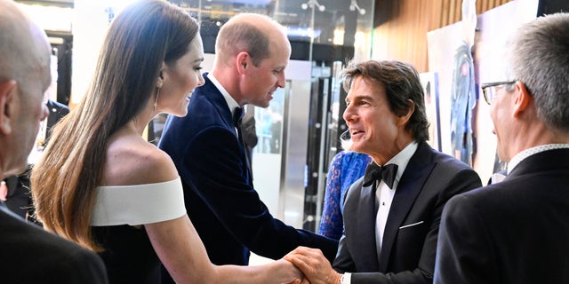 Tom Cruise holds Kate Middleton's hand with Prince William shaking hands in the background.