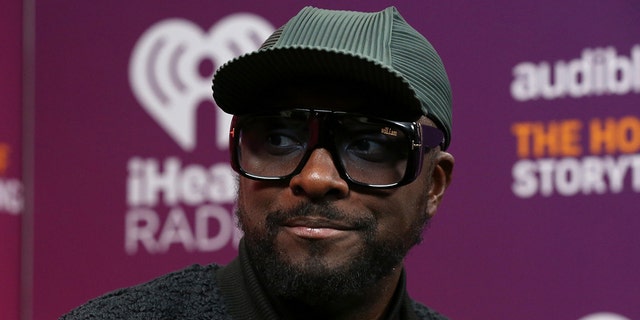 Will.I.am. wears a green hat at an IHeartRadio event and large glasses