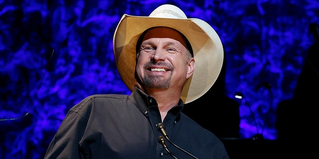 Garth Brooks smiles in a tan cowboy hat and black shirt onstage at the County Music Hall of Fame and Museum