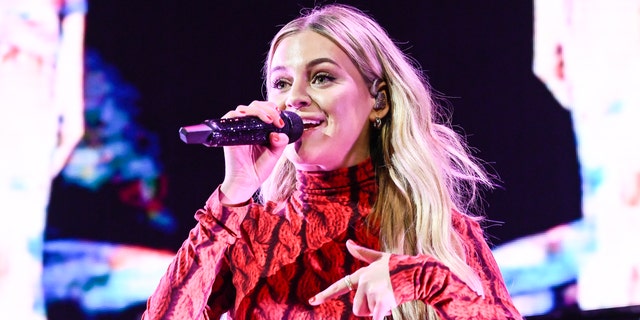 Kelsea Ballerini in a red patterned top singing into the microphone