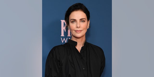 Charlize Theron with dark hair in a black shirt.