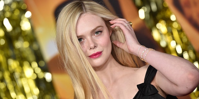 Elle Fanning on the red carpet puts her hand up to her hair and stares down the camera at the Babylon global premiere