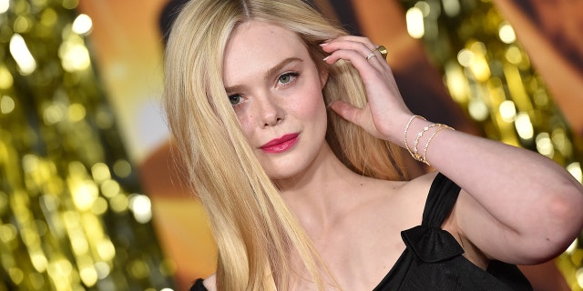 Elle Fanning on the red carpet puts her hand up to her hair and stares down the camera at the Babylon global premiere