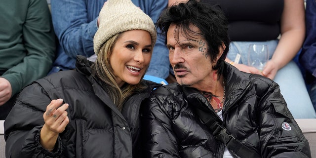 Brittany Furlan wears a beanie and black jacket while chatting with her husband Tommy Lee also in a black jacket at SoFi Stadium