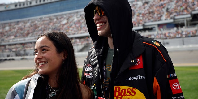 Pete Davidson in a black sweatshirt with logos smiles with girlfriend Chase Sui Wonders in Daytona Beach Florida for the NASCAR Cup Series