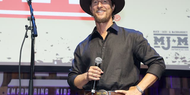 Matthew McConaughey on stage wearing a cowboy hat and holding a microphone