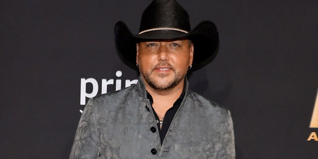 Jason Aldean smiles on the carpet in a black cowboy hat