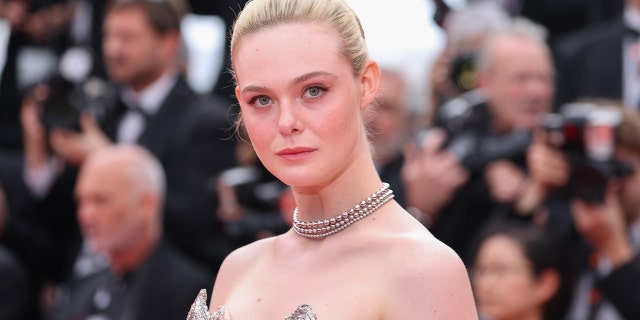 Elle Fanning smizes on the red carpet in Cannes wearing a strapless dress and a chain necklace