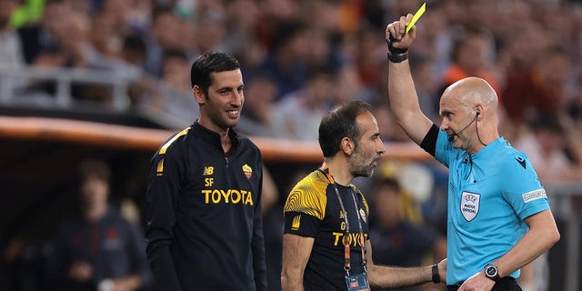 Anthony Taylor shows a yellow card to a Roma coach