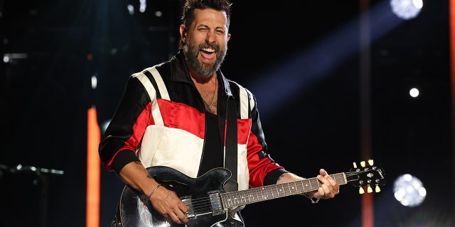 Matthew Ramsey strums the guitar in a black/red/white jacket while performing at CMA Fest with Old Dominion