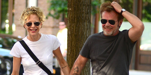 Meg Ryan in a white t-shirt laughs while holding hands with John Mellencamp on the streets of New York City