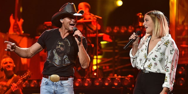 Tim McGraw in a black shirt and jeans and black cowboy hat sings on stage with daughter Gracie in 2015
