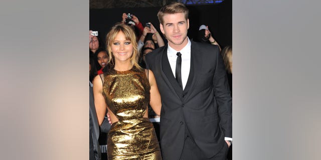 Jennifer Lawrence in a gold shimmery dress on the red carpet with Liam Hemsworth