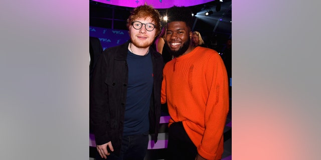 Ed Sheeran soft smiles wearing glasses for a photo with Khalid in red at the MTV Video Music Awards