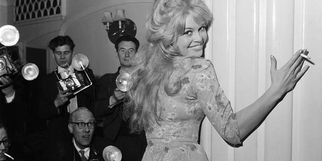 Brigitte Bardot embracing the wall as photographers stand nearby