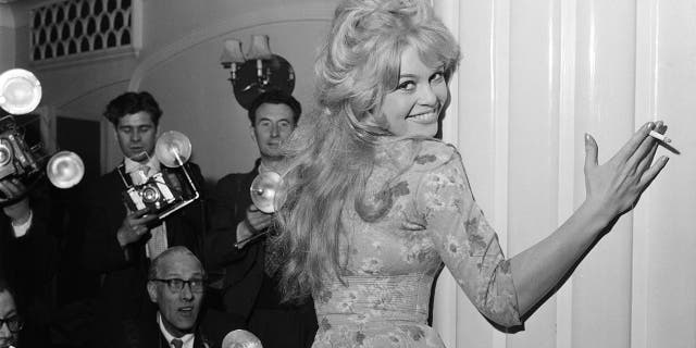 Brigitte Bardot embracing the wall as photographers stand nearby