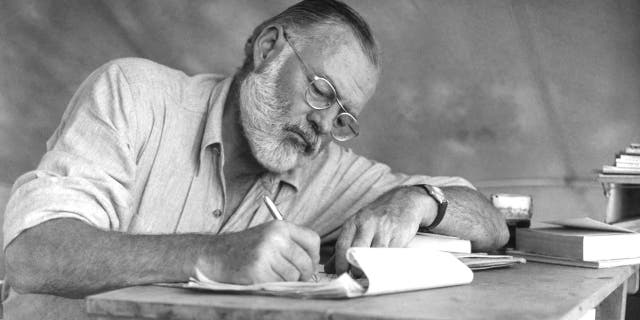 Ernest Hemingway writing on a notebook pad with a pen