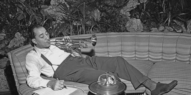 Louis Prima lounging on the couch while playing his trumpet