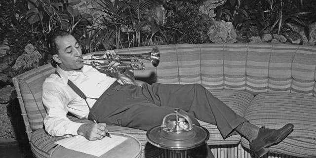 Louis Prima lounging on the couch while playing his trumpet