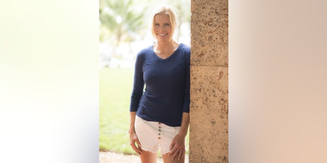 Mariel Hemingway in a long blue sleeved sweater and a white skirt