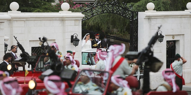 Crown Prince Hussein and Princess Rajwa in a car surrounded by red Land Rovers