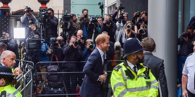 Prince Harry wearing a suit walking away from a crowd of photographers